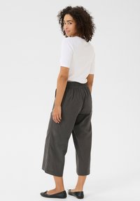 Pantalons noirs raccourcis avec une taille élastique, assortis à un haut blanc ajusté à manches courtes. Le mannequin a les cheveux bouclés et porte des ballerines noires.