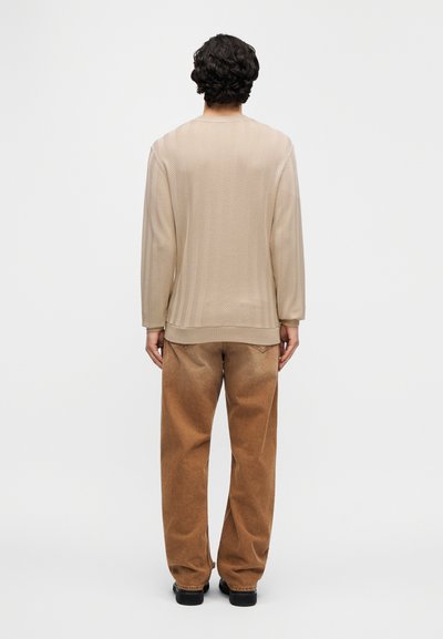 Μπεζ μακρυμάνικη μπλούζα με στρογγυλή λαιμόκοψη, συνδυασμένη με καφέ χαλαρά παντελόνια από κοτλέ. Το ντύσιμο έχει ένα διακριτικό σχέδιο ψαροκόκκαλου.