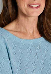 Hellblauer, gestrickter Pullover mit einem strukturierten Muster, weit ausgeschnittenem Halsausschnitt und glattem Stoff. Nahaufnahme des Halsausschnitts und der Schulterpartie.