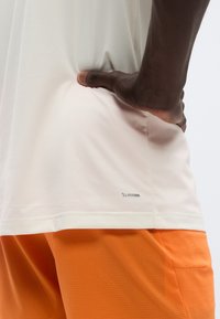 Άσπρο αθλητικό πουκάμισο με λεία υφή και λογότυπο ClimaCool στο τελείωμα, συνδυασμένο με πορτοκαλί σορτς με υφή μοτίβου.