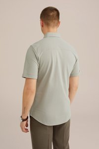 Camicia verde chiaro a maniche corte con colletto, caratterizzata da un orlo posteriore dritto e una texture liscia. Indossata con pantaloni marrone scuro.