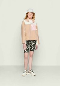 Pullover leve, com blocos de cor e meio fecho, em tons de rosa e bege, combinado com calções de cintura alta estampados e ténis desportivos.