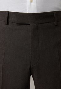 Dunkelbraune, maßgeschneiderte Hose mit strukturiertem Gewebe, flachem vorne und Gürtelschlaufen. Mit seitlichen Taschen und glatter Oberfläche.