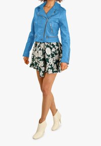 Modrá kožená zkrácená motocyklová bunda, květinová zelená sukně a bílé kotníčkové boty. Bunda má stříbrné zipy, na sukni je květinový vzor.