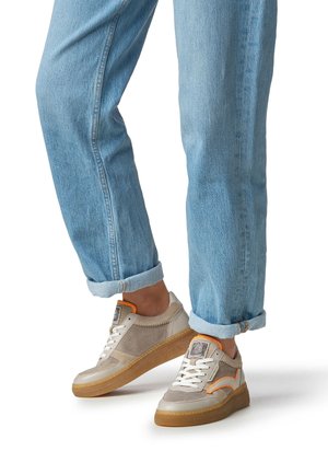 Veterschoenen met een beige bovenwerk van mesh en suède texturen, oranje accenten en een rubberen zool, gecombineerd met opgerolde blauwe jeans.