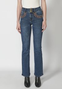 Blue denim jeans with a high waist, embellished pockets featuring colorful embroidery, and gold hardware. Fitted design, straight-leg cut.