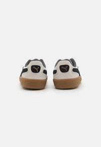 Puma joggesko med beige og svart fargekombinasjon, laget av semsket skinn og mesh-materialer, teksturert beige gummisåle og gulllogo-detall på hælen.