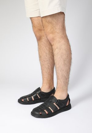 Les sandales en cuir noir présentent un design ouvert avec plusieurs brides, une semelle texturée et des accents contrastants pour la respirabilité et le style.