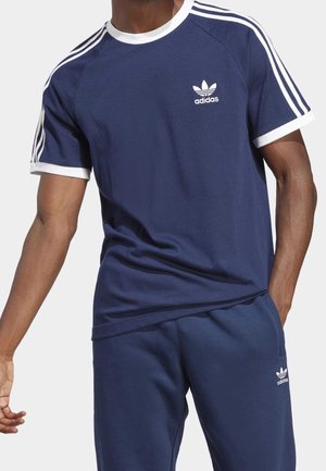 T-shirt de sport bleu marine avec bordure blanche et trois bandes blanches sur les épaules, arborant un petit logo Adidas blanc sur la poitrine.