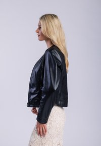 Černá kožená bomber bunda s přiléhavým střihem, zapínáním na zip a jemným leskem, spárovaná s texturovanou krémovou sukní.