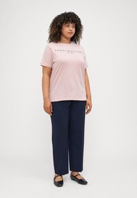 Svetloružové bavlnené tričko s čiernym logom "Tommy Hilfiger", skombinované s námorníckymi modrými voľnými nohavicami a čiernymi plochými topánkami.