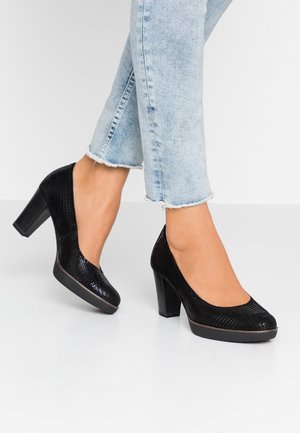 Zwarte plateauhakken met een textuur bovenkant, ronde neus en een chunky hak. Gemaakt in combinatie met lichtblauwe, versleten jeans. Het oppervlak heeft een glanzende afwerking.