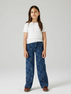 T-shirt blanc à manches courtes associé à un jean large à motif floral bleu et des chaussures marron. Les jeans présentent un design de rose subtil.