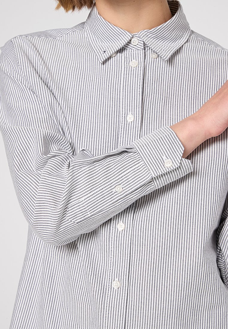 Camicia a righe con colletto classico, bottoni bianchi e maniche lunghe con polsini. Il tessuto è leggero e testurizzato.