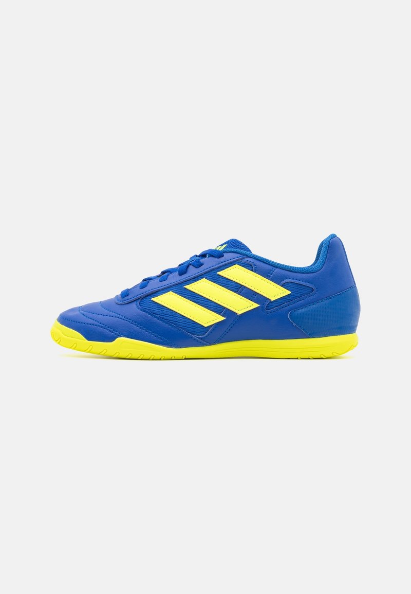 Baskets de soccer en intérieur bleues avec une semelle jaune et trois rayures jaunes sur le côté, sur fond blanc.