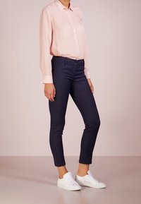 Camisa de botón rosa claro con mangas largas, combinada con pantalones ajustados azul marino y zapatillas blancas. Tejido suave, diseño a medida.