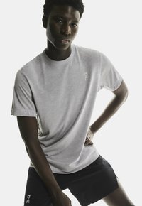 Lysegrå kortærmet t-shirt lavet af glat stof, med et diskret logo på brystet. Kombineret med sorte træningsshorts.