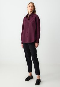Bordeaux knopenoverhemd met een kraag, één borstzak, lange mouwen en een relaxte pasvorm, gecombineerd met zwarte slim-fit broek en instappers.