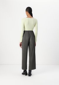 Haut à manches longues vert côtelé associé à un pantalon gris foncé à taille haute et plis. La tenue présente une coupe décontractée et une longueur au niveau des chevilles.
