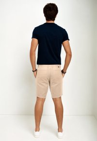 Marineblaues T-Shirt mit kurzen Ärmeln, kombiniert mit beigen Shorts und weißen Sneakers. Die Shorts haben eine klassische Passform mit zwei Gesäßtaschen.