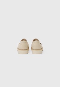 Chaussures en suede beige avec un petit talon, un dos arrondi et des détails de couture minimalistes. Texture lisse et design simple sans ornements.