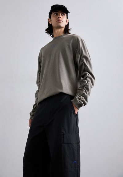 Maglietta grigia a maniche lunghe con maniche arricciate, abbinata a pantaloni cargo neri larghi con una grande tasca a toppa e un accento blu con logo.