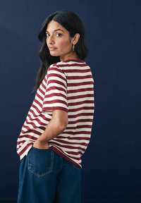 Gestreiftes T-Shirt in Rot- und Cremetönen, mit kurzen Ärmeln, lässiger Passform und Rundhalsausschnitt, kombiniert mit blauen Jeans.