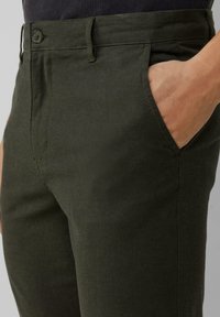 Broek in donkergroene stof met een gladde textuur. Beschikt over een voorzak en een knoopsluiting bij de taille. Klassiek getailleerd ontwerp.
