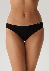 Czarne majtki bikini o minimalistycznym designie, z niskim stanem, gładką teksturą i małą metką logo z boku.