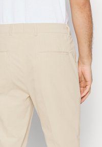 I pantaloni in corduroy beige presentano una texture liscia, due tasche posteriori e un design a gamba dritta. La cintura è dotata di passanti per la cintura per una vestibilità regolabile.