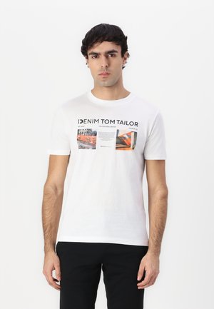 Camiseta de algodón blanca con estampados gráficos a color, cuello redondo y mangas cortas. Se lleva con pantalones negros.