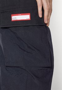 Main reposant sur une veste noire montrant une étiquette rouge avec le texte « AIR », « #23 », « Michael Jordan » et « Beaverton, OR USA ».