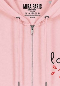 Felpa con zip in cotone rosa, dotata di zip argentata e testo nero con accenti rossi. Include istruzioni per la cura stampate all'interno del cappuccio.