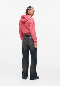 Rozā cropped hoodie ar kapuci, pārī ar tumši ziliem platām biksēm. Tērps ietver šūšanas detaļas un jostas etiķeti.
