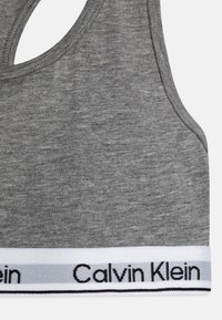 Top sportivo grigio in cotone con scollatura a barca e un elastico con la scritta "Calvin Klein" in bianco e nero. Tessuto morbido, design aderente.