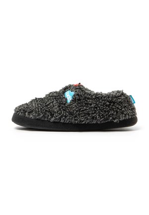 Una única zapatilla gris y peluda con suela negra y etiquetas de tela azules y rojas, mostrada de lado sobre fondo blanco.