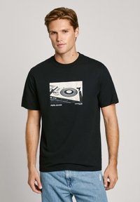 Juodas medvilnės marškinėliai su grafika, vaizduojančia garso plokštelę ir stiklinę, su tekstu "PEPE JEANS" apačioje. Standartinio apvalaus kaklo dizainas.