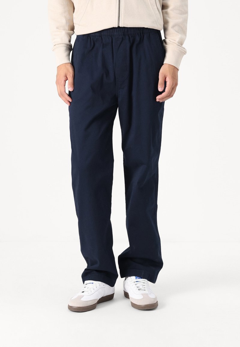 Marinblå, lätta byxor med elastisk midja och avslappnad passform, tillverkade av ett mjukt tyg, kombinerat med vita sneakers.