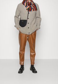 Grå stickad cardigan med knappar, flerfärgad randig scarf, bruna läderbyxor och svarta loafers, kompletterad med en liten svart crossbody-väska.