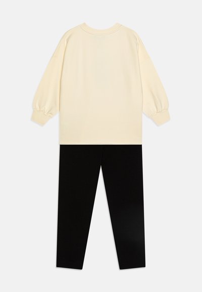 Felpa color crema con maniche a sbuffo abbinata a leggings neri. Il tessuto sembra morbido, con un design semplice e senza decorazioni.