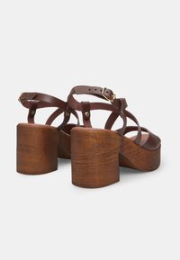 Brown leather platform sandals with thick wooden block heels, featuring intersecting straps and adjustable ankle buckle detail.