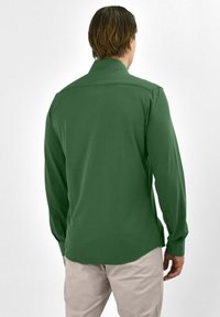 Langsleevige, effen groene shirt in een gladde stof met een getailleerde pasvorm, voorzien van een klassieke kraag en knoopmanchetten.