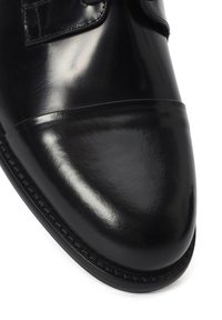 Zwarte gepolijste leren veterschoen met decoratief stiksel en cap-toe ontwerp op witte achtergrond.