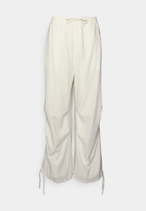 Lockere weiße Baumwollhose mit elastischem Bund und Kordelzug an Taille und weiten Beinen vor hellem Hintergrund.