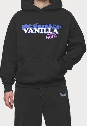 Osoba ubrana w czarną bluzę z kapturem z napisem "pegador VANILLA Super Soft!" w kolorach niebieskim, białym i różowym na piersi oraz czarne spodnie z małym logo.