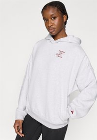 Siva kapuca z mehkim materialom. Na prsih majhen rdeč logotip in rdeč detajl na manšetni. Ohlapen kroj.