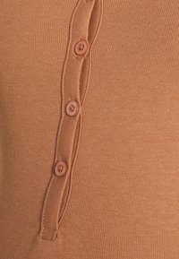 Top canelado em cor ferrugem, apresentando uma linha de quatro botões redondos e rosados na parte da frente, com uma textura subtil e detalhes curvos ao lado dos botões.