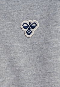 Petit patch brodé d'abeille blanche et bleu marine sur fond de tissu tricoté gris clair.