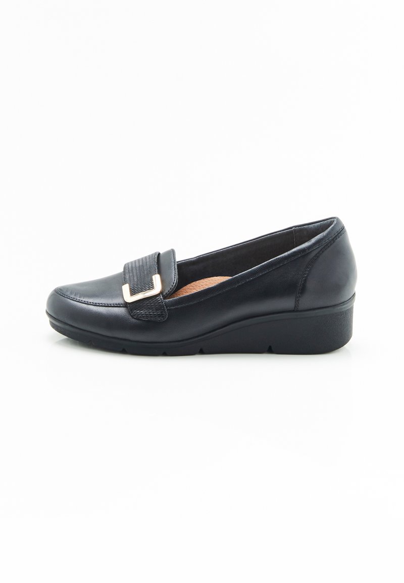 Zapato de vestir negro de cuero sin cordones con una correa texturizada y hebilla de metal dorado, que presenta una suela de cuña baja y plantilla acolchada.