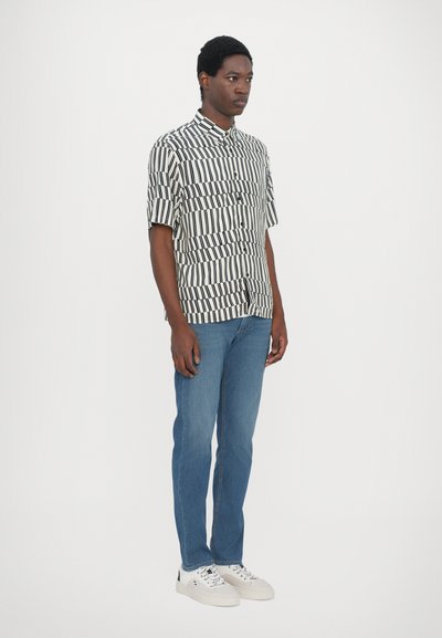 Short-sleeve button-up shirt in striped black and white pattern, paired with slim-fit blue jeans and white sneakers with gray accents.
